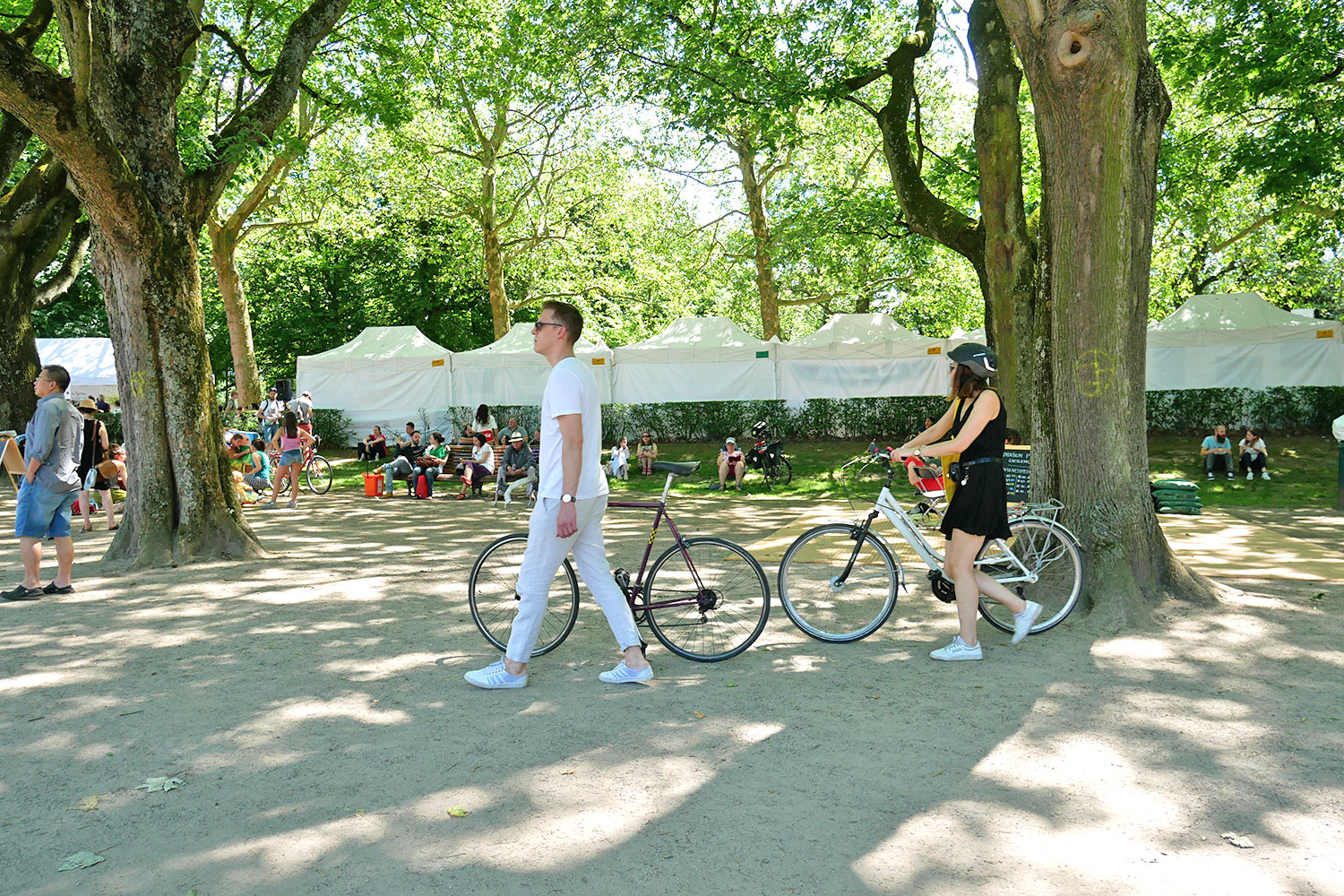 2 cyclistes marchant à pied avec leur vélo à leur côté dans un parc